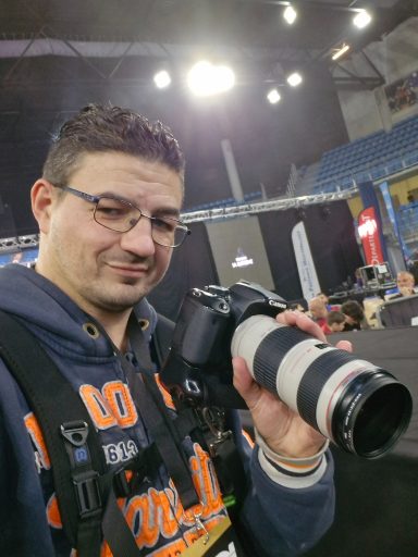 Homme prenant une photo avec un appareil photo reflex, souriant et en arrière-plan flou.