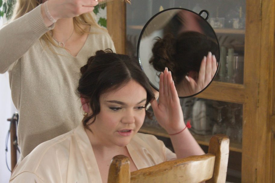 Une femme se coiffe avec l'aide d'une coiffeuse devant un miroir.